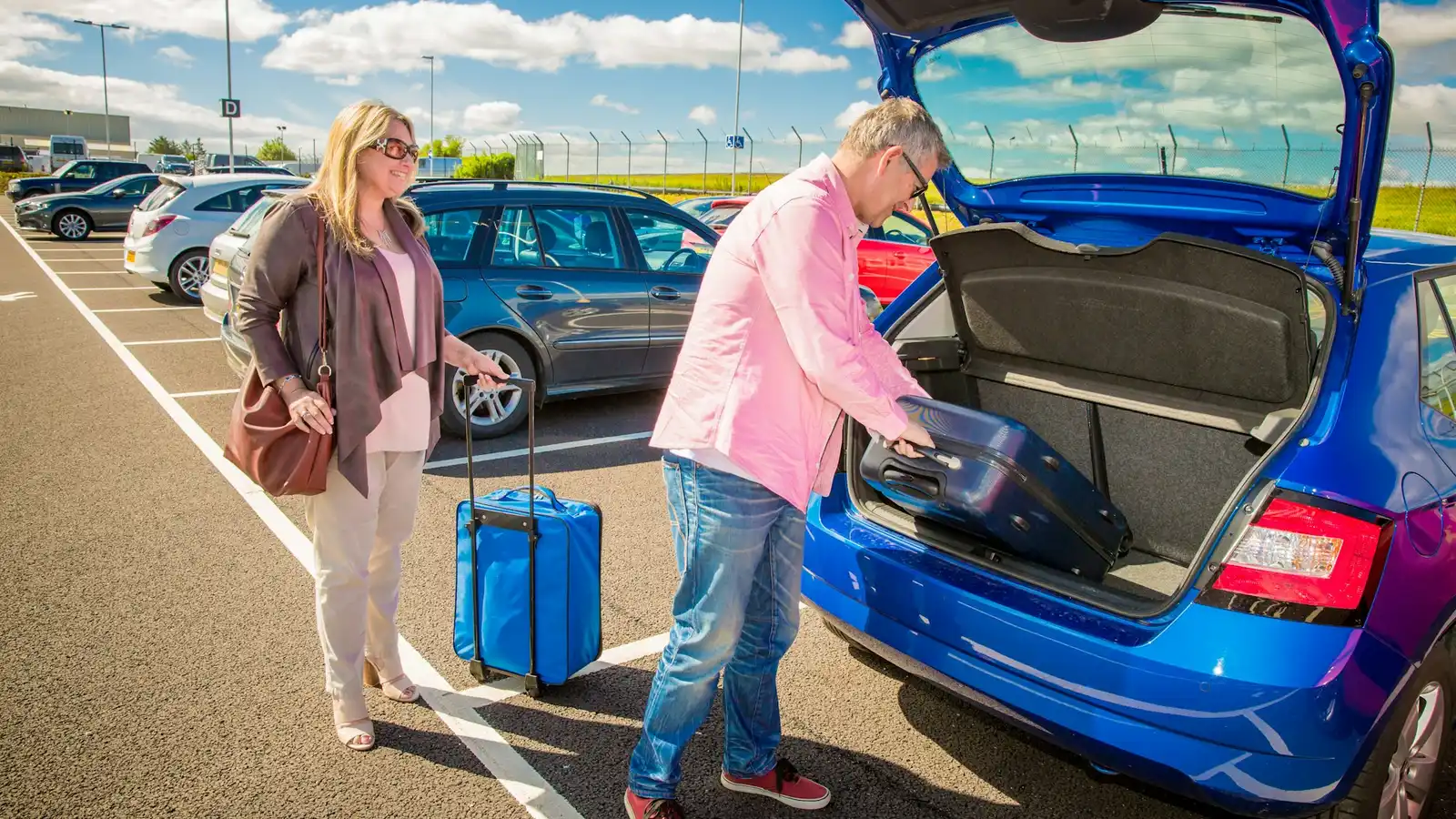 Travellers loading suitcases into a car at an airport car park