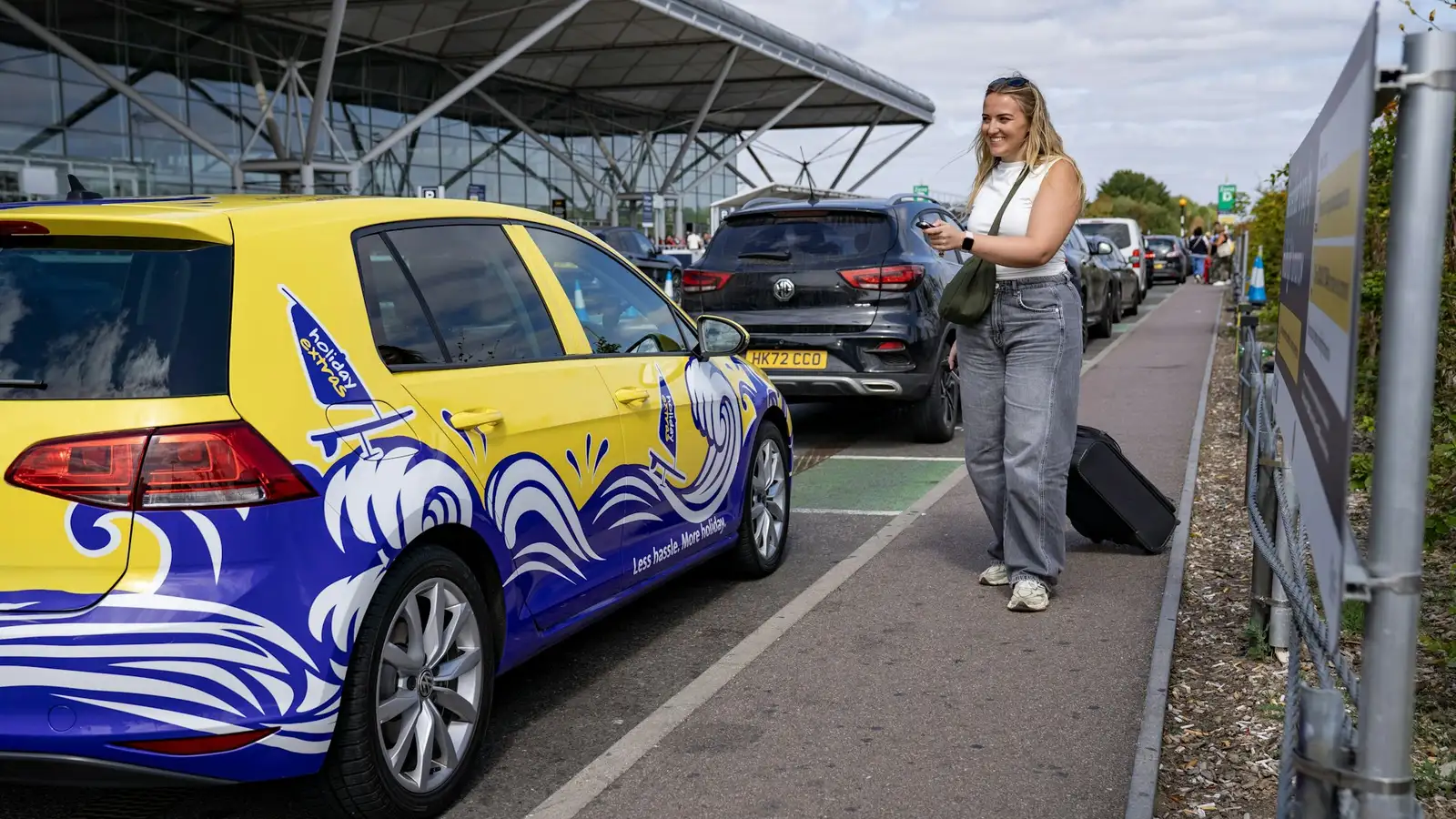A traveller with her suitcase beside a car on the Stansted Airport forecourt